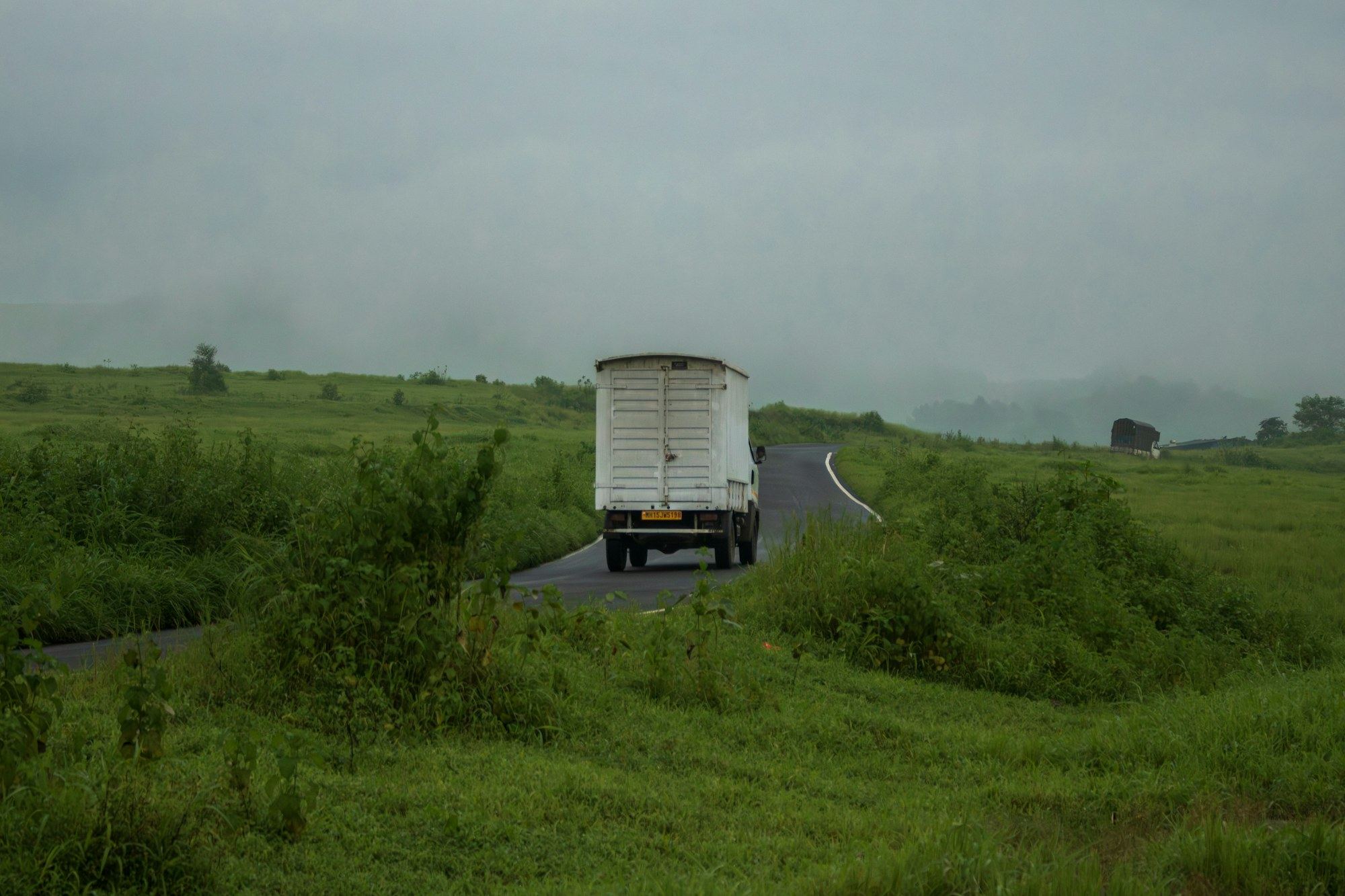White dry van truck heading down a rural two-lane road in morning mist
